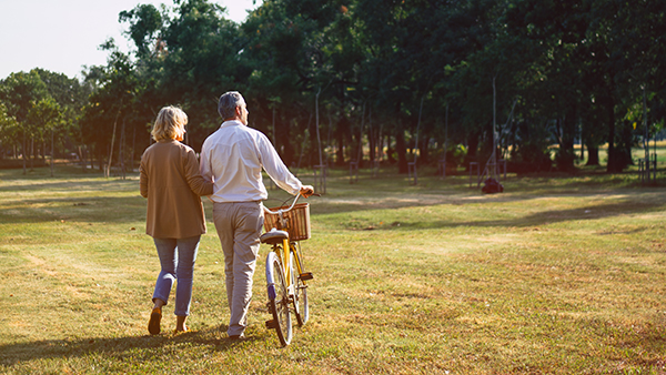A senior couple walks through a field walking a bike as they go. At G2 Orthopedics, Dr. Vic Goradia serves many active adults like this couple.